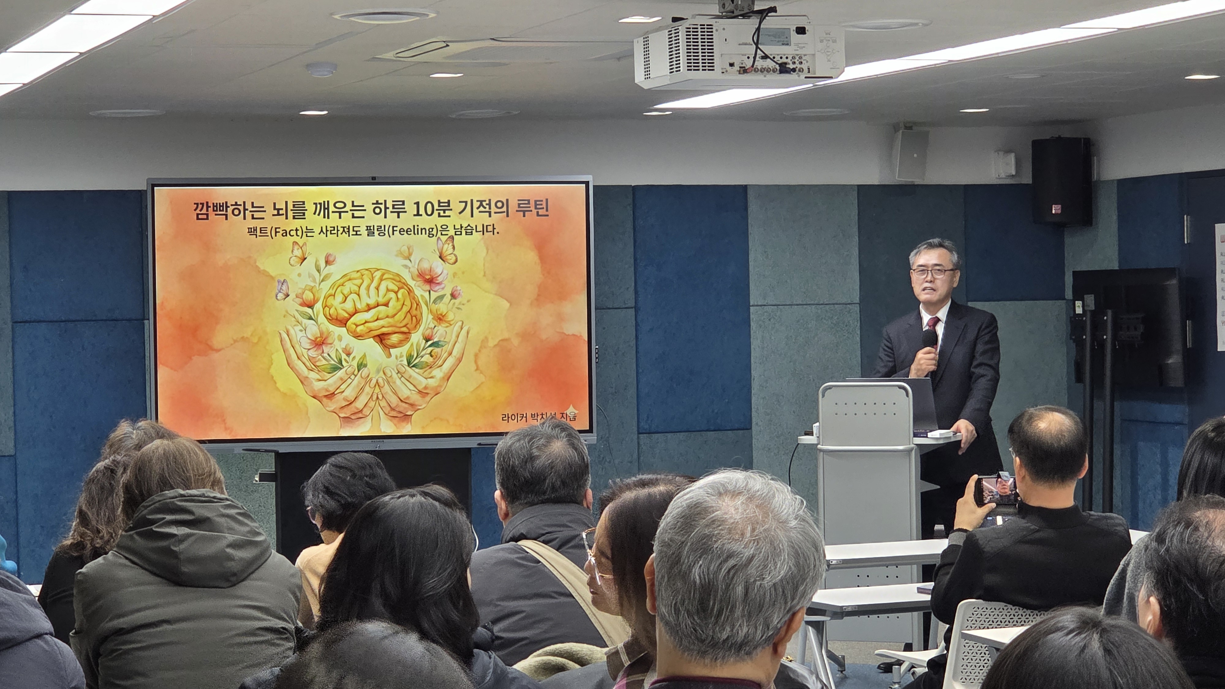 마포 플랫폼P 다목적실 — 파란색 어쿠스틱 패널 벽, 길게 배치된 흰색 책상에 30~40명이 앉아 강연을 듣는 모습